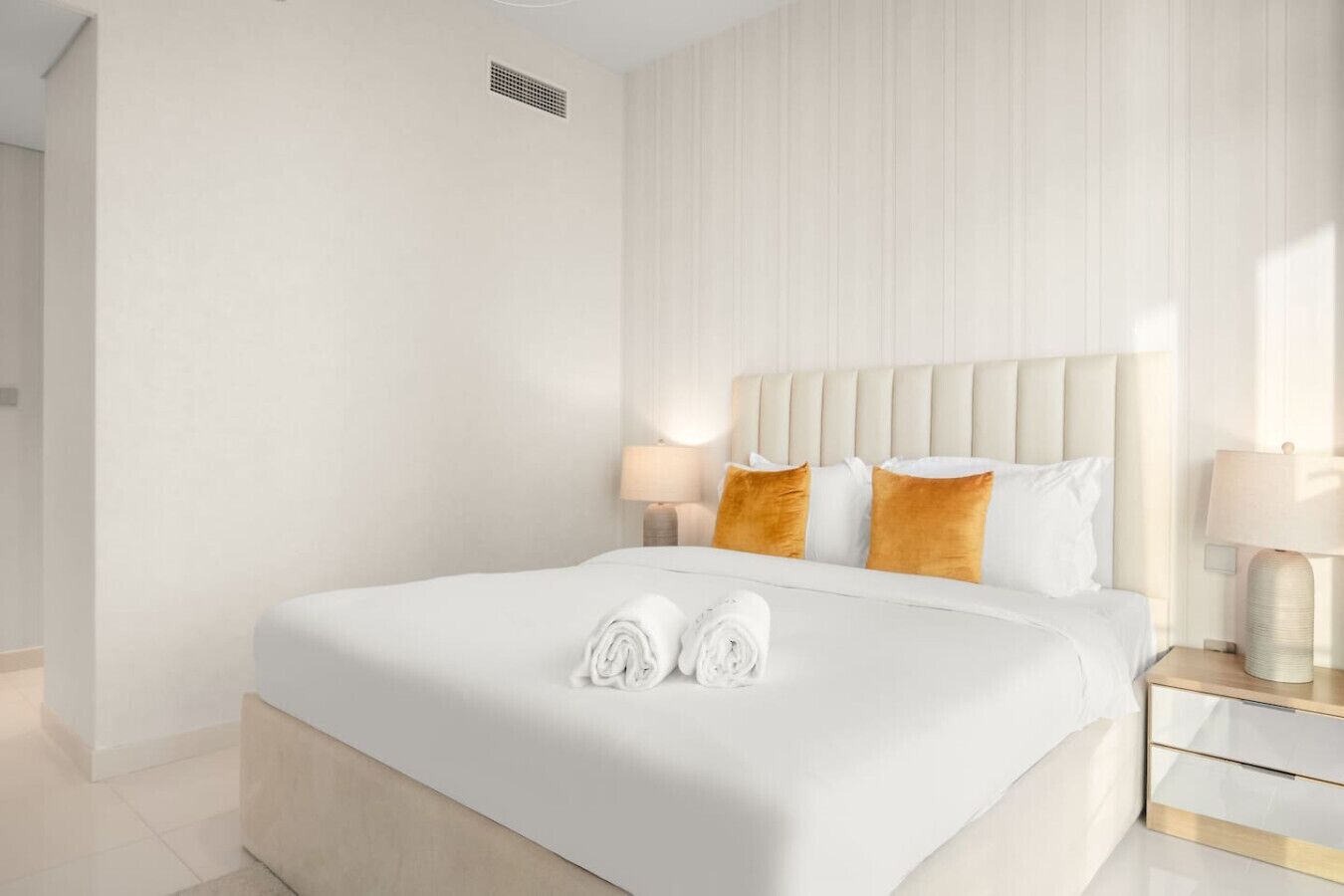 Une chambre d’hôtel avec un grand lit, une tête de lit, deux tables de chevet et une lampe.