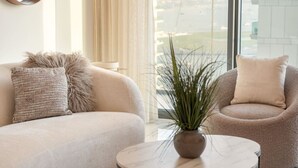 A modern living room with a beige sofa, a round coffee table, and a chair with a plant on it. - FIRST CLASS | 2BR | Sea & Palm View | Beachfront (Dubai)