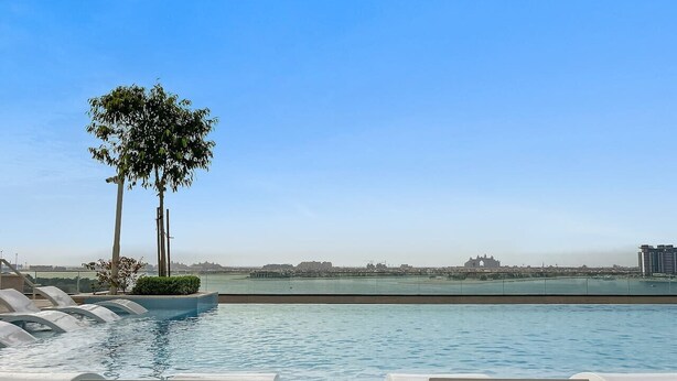 A swimming pool with lounge chairs and a view of the city skyline. - FIRST CLASS | 2BR | Sea & Palm View | Beachfront (Dubai)