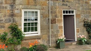A stone house with a tiled roof, two windows, a door, and a small garden with flowers. - Stunning  villa for 4 people with WIFI, TV and terrace (Ingleby Greenhow)