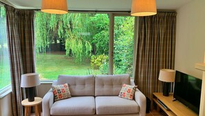 A living room with a sofa, two lamps, a TV, and a large window with curtains. - Stunning  villa for 4 people with WIFI, TV and terrace (Ingleby Greenhow)
