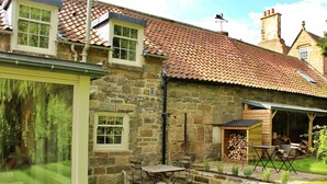 A stone house with a tiled roof, a patio with a table and chairs, and a garden area with a wooden shed. - Stunning  villa for 4 people with WIFI, TV and terrace (Ingleby Greenhow)