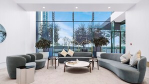 A modern living room with a large window, grey sofas, a coffee table, and a trash bin.