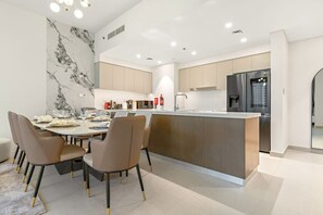 A modern kitchen with a central island, built-in appliances, and a dining area with a marble backsplash.