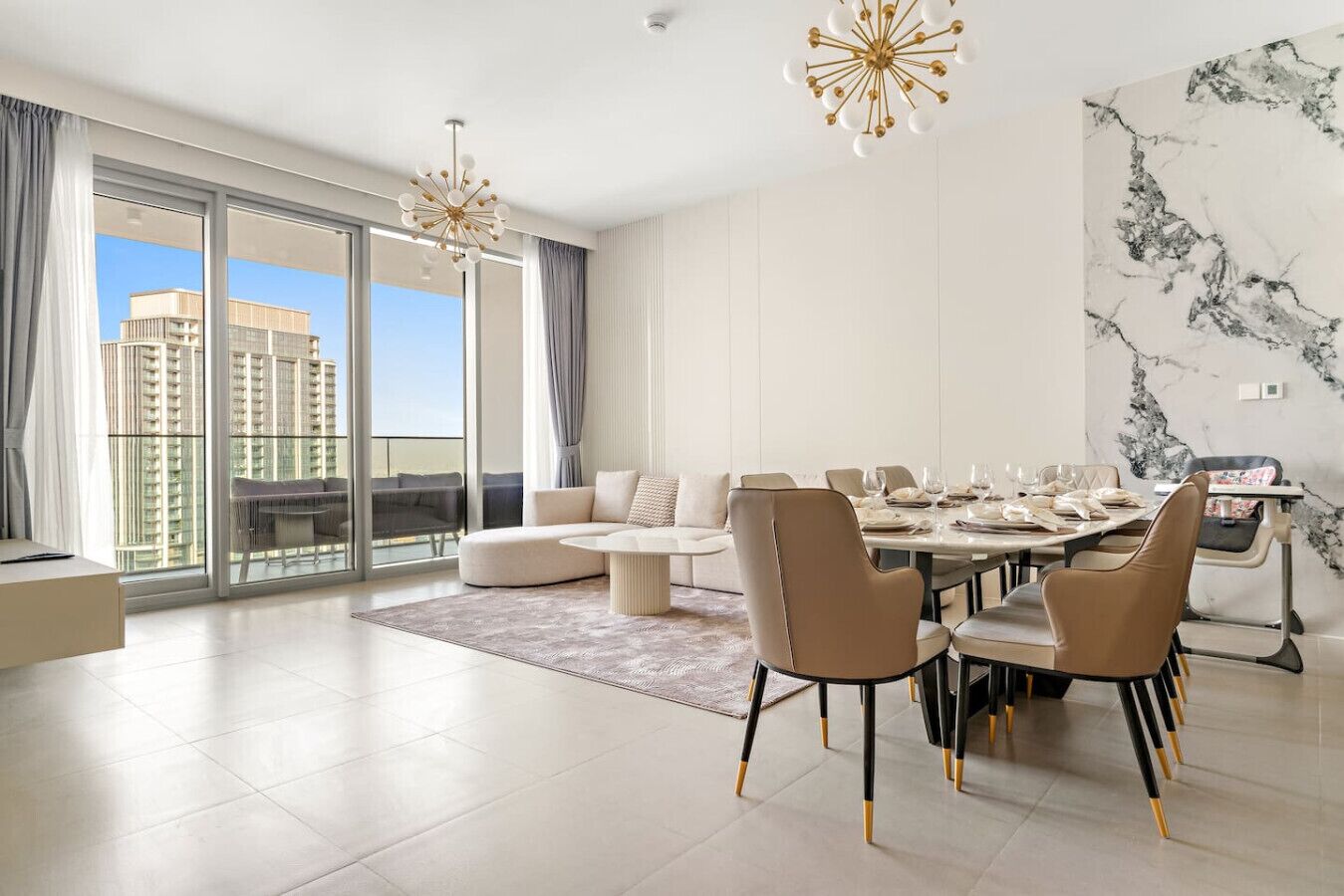 A modern living room with a dining area, large windows, and a view of high-rise buildings.