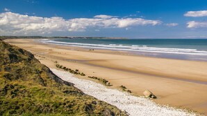 Paisagem costeira com uma extensa praia de areia, litoral rochoso e céu azul límpido.
