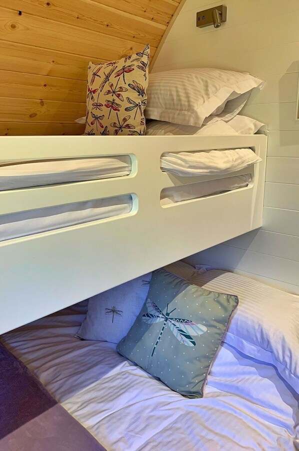 A bunk bed with a wooden ceiling, white bedding, and patterned pillows.
