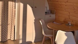 Ein gemütliches Zimmer mit Holzbalkendecke, einem weißen Kleiderschrank, einem kleinen Tisch mit Stühlen und einem gemusterten Vorhang.
