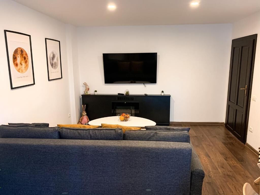 Una sala de estar moderna con un sofá gris grande, una mesa de centro redonda blanca y un televisor de pantalla plana montado en la pared.