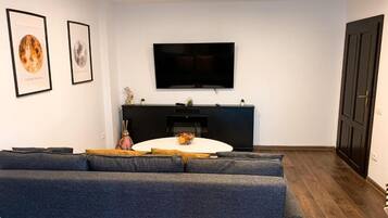 Una sala de estar moderna con un sofá gris grande, una mesa de centro redonda blanca y un televisor de pantalla plana montado en la pared.