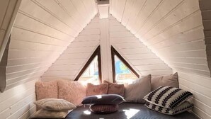 Une chambre mansardée chaleureuse avec un plafond en pente, un lit avec des oreillers et une petite table sur laquelle est posée une bougie.