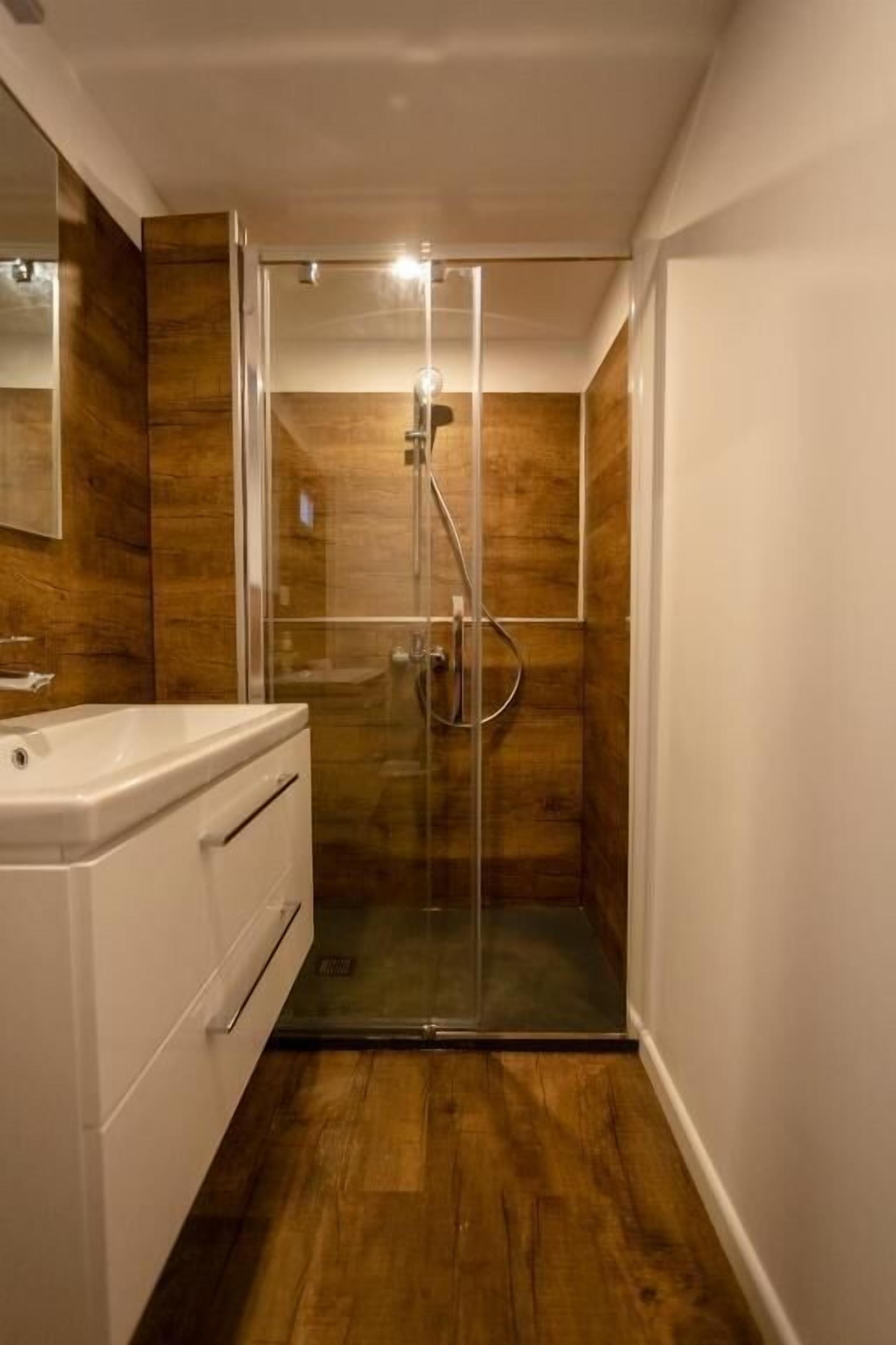 A modern bathroom with a glass-enclosed shower, a white vanity, and wooden flooring.