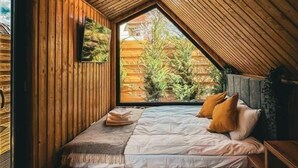 Une chambre mansardée chaleureuse avec un plafond en pente, des murs en bois, un lit avec des oreillers, une fenêtre et une petite table.