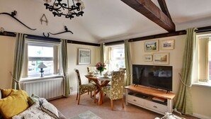 Ein gemütliches Wohnzimmer mit einer Couch, einem Esstisch mit Stühlen, einem Fernseher und einer Pendelleuchte.