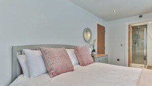 A bedroom with a bed, a bedside table, a mirror, and a door leading to a shower area.
