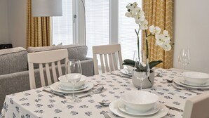 A dining area with a table set for four, a sofa, a lamp, and a window with curtains.