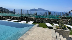 A pool with clear water, white lounge chairs, and a view of the sea and mountains.