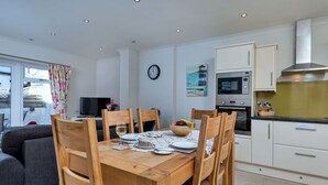 A modern kitchen with white cabinets, a microwave, and a stove. There is a dining table with chairs and a clock on the wall.