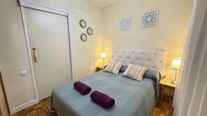 A bedroom with a bed, two bedside tables, a nightstand, a door, and wall decor.