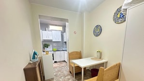 A compact kitchen with white cabinets, a small dining table, and a wooden bench. - Habitaciones en Luisa (Madrid)