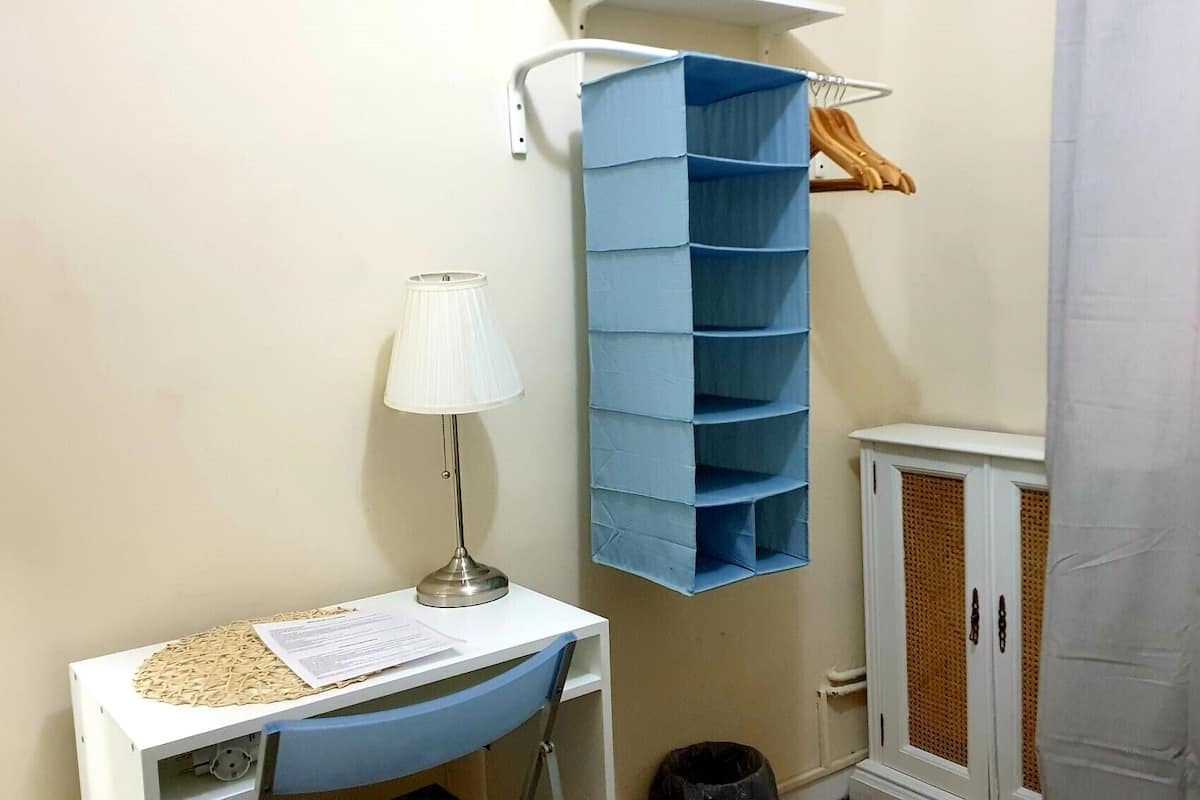 A room with a white desk, a blue storage unit, a white lamp, and a white cabinet with a wicker basket.