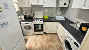 A compact kitchen with white cabinets, a washing machine, a stove, and a sink. - Habitaciones en Luisa (Madrid)