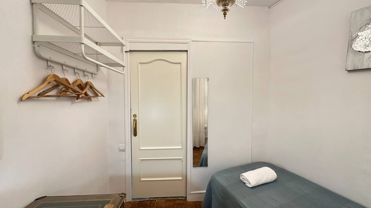 Quarto com cama, porta, espelho e prateleira fixada na parede com cabides.