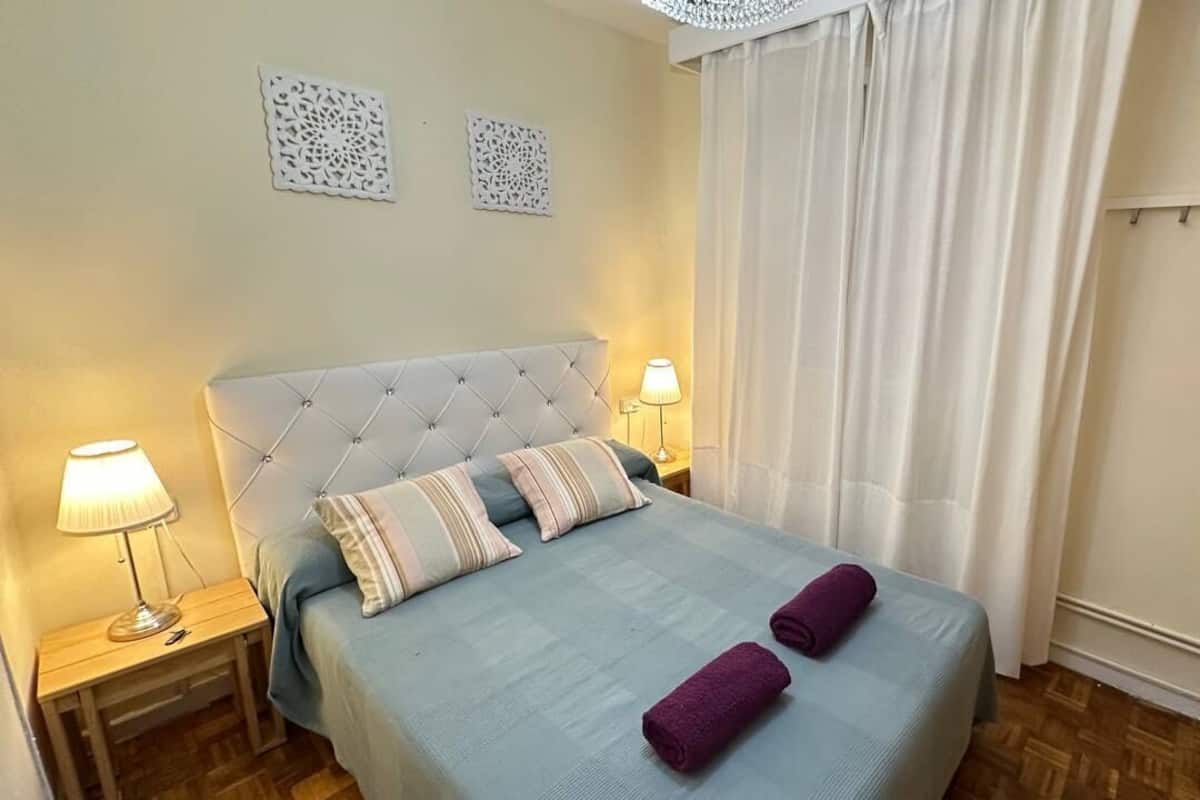 A bedroom with a bed, two nightstands, a wardrobe, and a window with curtains.