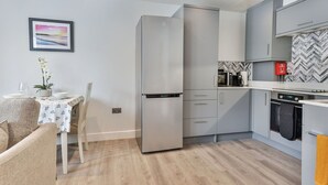A modern kitchen with a built-in refrigerator, microwave, and oven. There is a dining area with a table and chairs, and a small plant on the table. - Nice apartment for 2 people with WIFI, TV and pets allowed (Filey)
