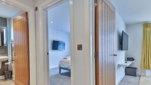 A modern hotel room with a wooden door, a bed, a TV, and a small desk with a speaker. - Nice apartment for 2 people with WIFI, TV and pets allowed (Filey)