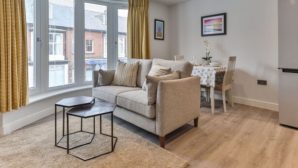 A modern living room with a sofa, a coffee table, and a dining area with a table and chairs. - Nice apartment for 2 people with WIFI, TV and pets allowed (Filey)