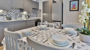 A modern kitchen with grey cabinets, a herringbone backsplash, and a built-in oven. There is a dining area with a table set for four, white chairs, and a potted orchid. - Lovely apartment for 4 people with WIFI and TV (Filey)
