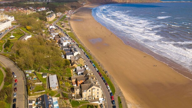 A coastal town with a sandy beach, a promenade lined with parked cars, and a mix of residential and commercial buildings. - Lovely apartment for 4 people with WIFI and TV (Filey)