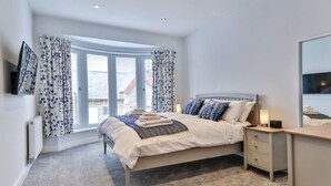 A bedroom with a bed, bedside tables, a TV, and a window with curtains. - Lovely apartment for 4 people with WIFI and TV (Filey)