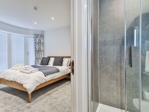 A bedroom with a bed, a glass shower enclosure, and a window with blinds.