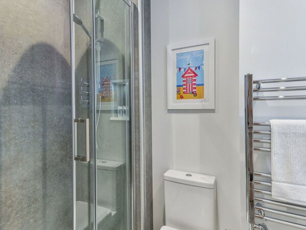 A bathroom with a glass shower enclosure, a white toilet, and a towel rack with a white towel.