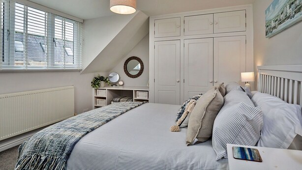 Une chambre avec un grand lit, un luminaire au plafond, une fenêtre avec des stores, un radiateur et une armoire.