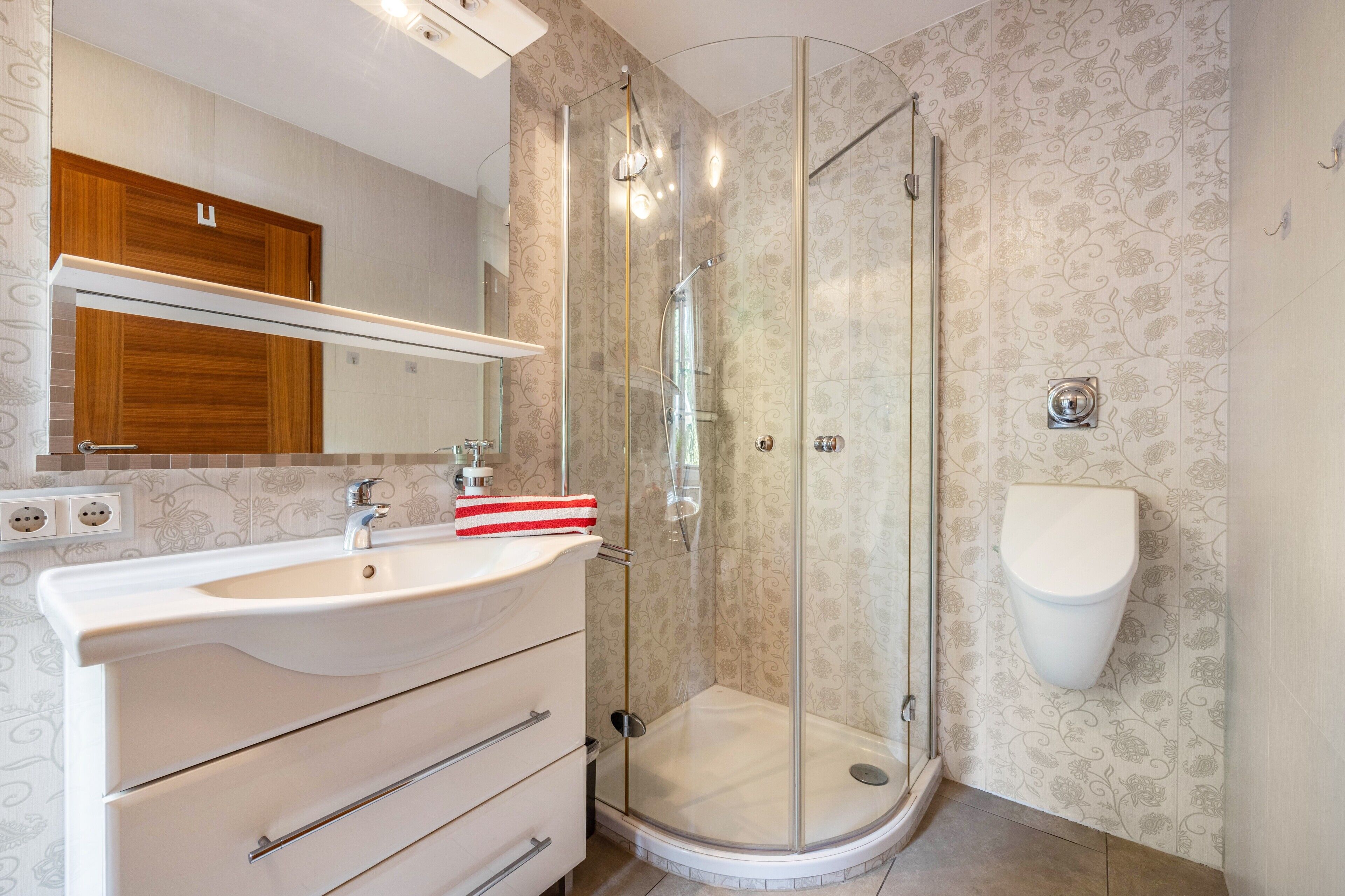 Een badkamer met een douchecabine van glas, een wit wastafelmeubel en een toilet.