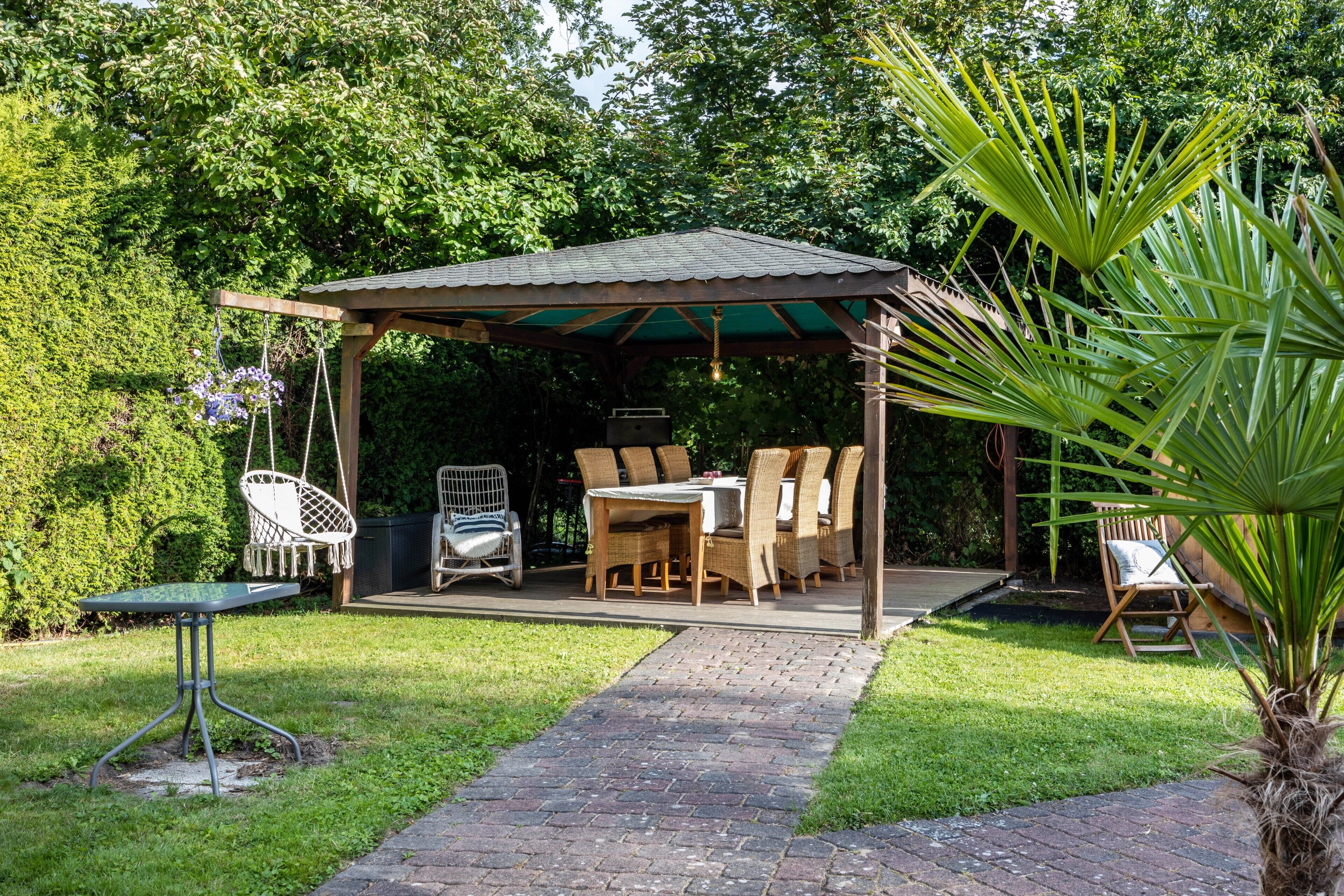 Une terrasse couverte, dotée d’une table et de chaises, et entourée de verdure.