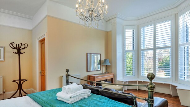 A hotel room with a large bed, a desk, a chair, a coat stand, and a window with blinds. - Stunning  villa for 10 guests with WIFI, TV and pets allowed (Whitby)