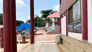 A covered outdoor area with red pillars, a tiled floor, and a building with a red and white facade. - Royal Lee's Hotel (Tutu)