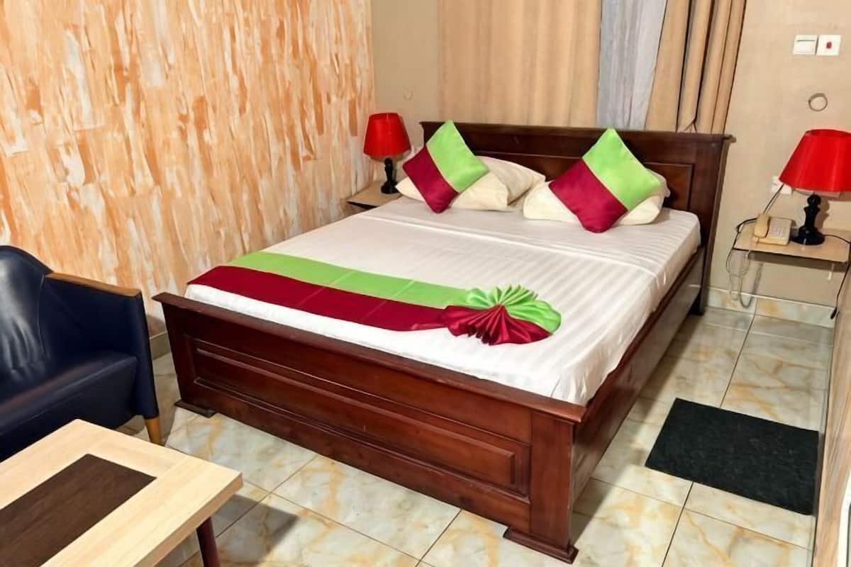 Una habitación de hotel con una cama de madera, un escritorio, una silla y una mesita de noche con lámpara.
