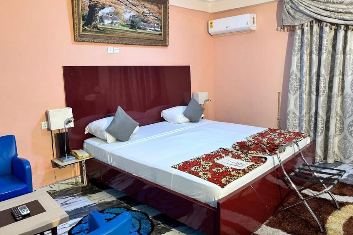 Habitación de hotel con una cama grande, una mesita de noche con lámpara, una silla y una pequeña mesa con teléfono.