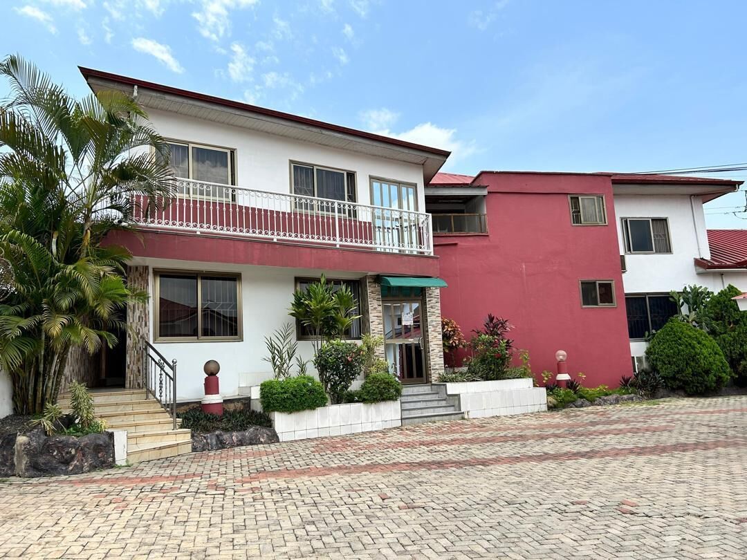Una casa de dos pisos con balcón, fachada roja y blanca, y camino de entrada pavimentado.