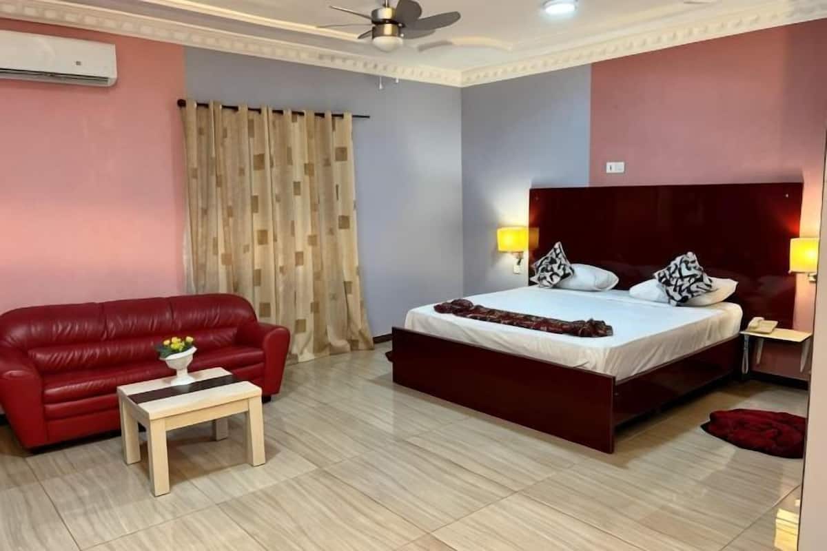 Un dormitorio con cama, sofá rojo, mesita y ventilador de techo.
