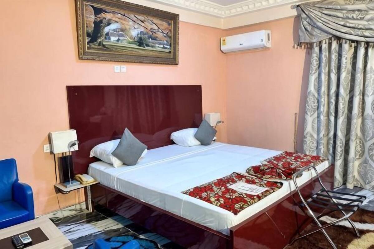 Habitación de hotel con cama, lámparas de noche, una silla, escritorio y un cuadro en la pared.