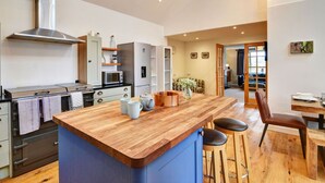 Een moderne keuken met een centraal eiland, houten barkrukken, en een eethoek met een tafel en stoelen.