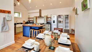 Een ruime keuken met een centraal kookeiland, houten barstoelen en een eethoek gedekt voor een maaltijd.