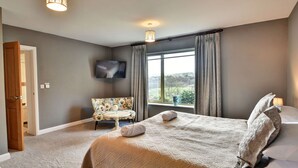 Een slaapkamer met een groot bed, een bank, een televisie en een raam met gordijnen.
