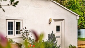 Una casa blanca con puerta y ventanas, rodeada de follaje y una terraza de madera.